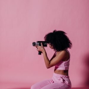 Side view of African American woman in pink outfit using vintage camcorder in a studio setting.